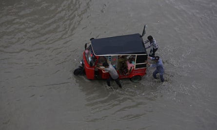 People push a rickshaw through a flooded road after a heavy rainfall in Karachi, Pakistan