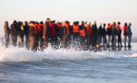 Large group of people wearing life vests stand in the shallows on French beach.
