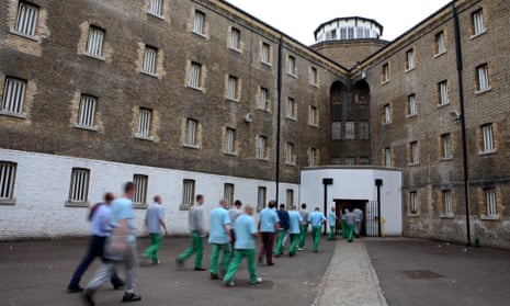 A group of prisoners walk across a yard and enter a prison building
