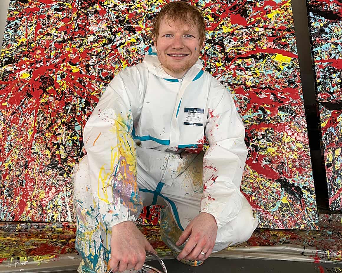 Ed Sheeran in a white, painted-stained overall in from of an abstract painting