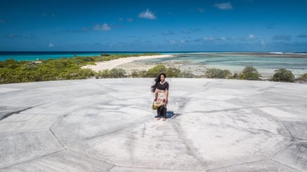 A woman stands in a woven grass costume on a concrete dome on an atoll