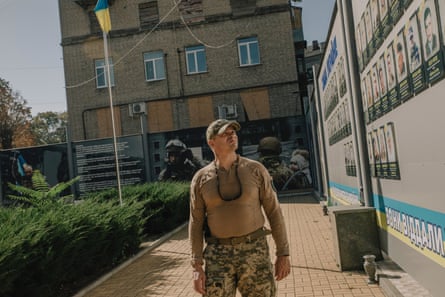 Man in military fatigues looks to his left at a board displaying images of fallen soldiers