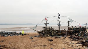 New Brighton, England: A man walks his dog by the Black Pearl driftwood pirate ship