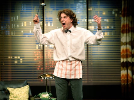 A man in a white shirt with a bow tie and a red and white stripy apron holding his hands up in the air