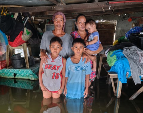 A family of five stand knee-deep in their flooded house, the tables piled high with their belongings