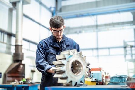 A young male apprentice engineer cleans gear for a pump in an electrical engineering factory.