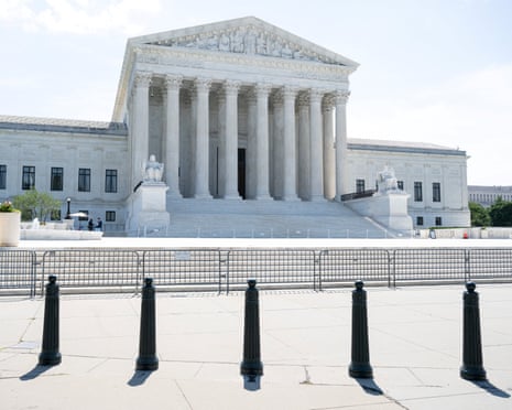 The white columned facade of the US Supreme Court building behind metal barricades and bollards