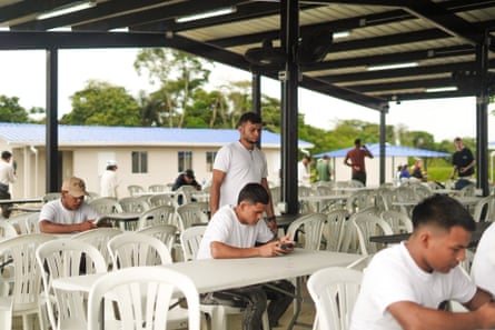 Men sit at tables under a canopy looking at their phones