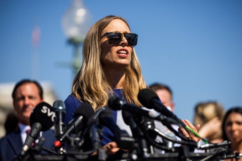 person wearing sunglasses speaks into a bunch of microphones outside