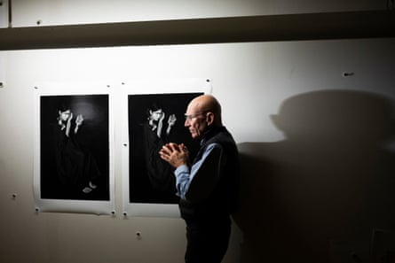Sebastião Salgado stands with his right side against a wall on which is pinned two versions of the same photograph