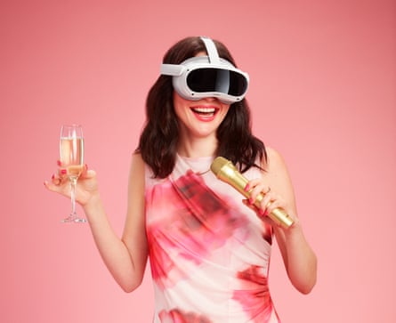 A woman with long dark hair wearing a pink patterned sleeveless dress and a VR headset, and holding a gold microphone and a glass of sparkling wine
