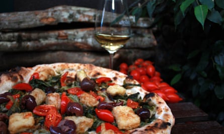 Olive pizza and a glass of wine on a table at Pizza Da Attilio, Napes, Italy.