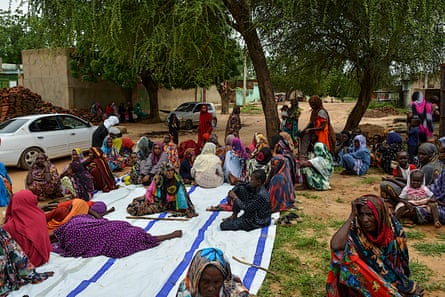 women and children sit in the shade of a tree waiting to be seen at a clinic