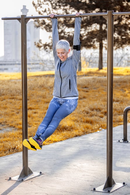 Older woman hanging on gymnastic bar in park