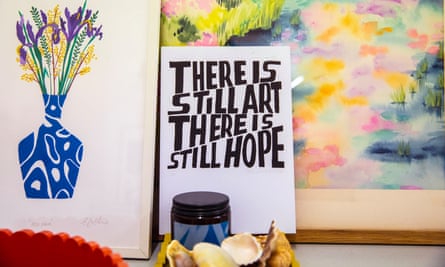 A painting of flowers in a narrow-necked vase next to art reading “There is still art. There is still hope” in front of an abstract painting
