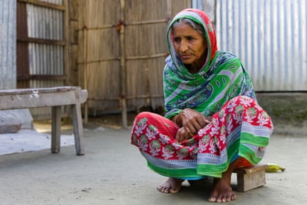 An older Indian woman in a sari squats on the ground in a yard