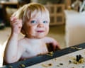 A blond-haired toddler sitting at a table covered in food which is all over the table in front of him