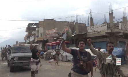Armed Houthi fighters raise their automatic rifles in the air as they walk through a street