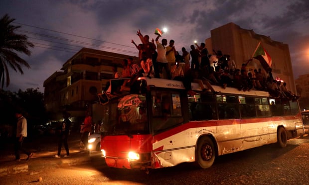 Sudanese people celebrate on top of a bus