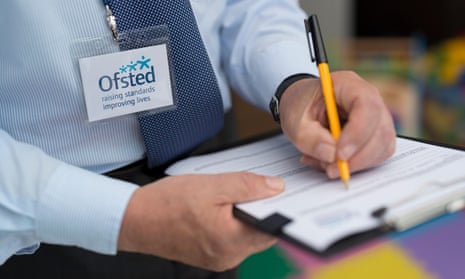 A man dressed with an Ofsted lanyard appears to be compiling a report using a pen and clipboard