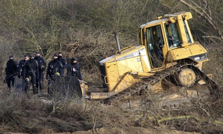 Police officers walk past a bulldozer in the Calais refugee camp, used to clear a 100m-long strip of land between the camp and the highway.