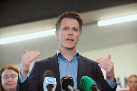 A man with raised hands speaks before a bank of microphones.