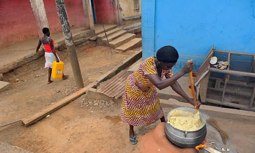 A woman prepares the West African dish fufu in the street with a large pestle and mortar.