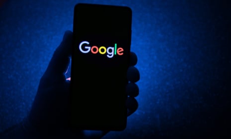 Hand is holding a smartphone with the Google logo displayed and dark blue background.