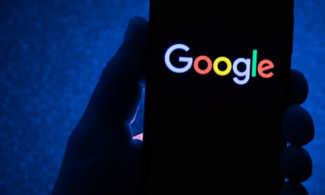 hand in shadow holding a smartphone with the multicoloured Google logo displayed against a dark blue background