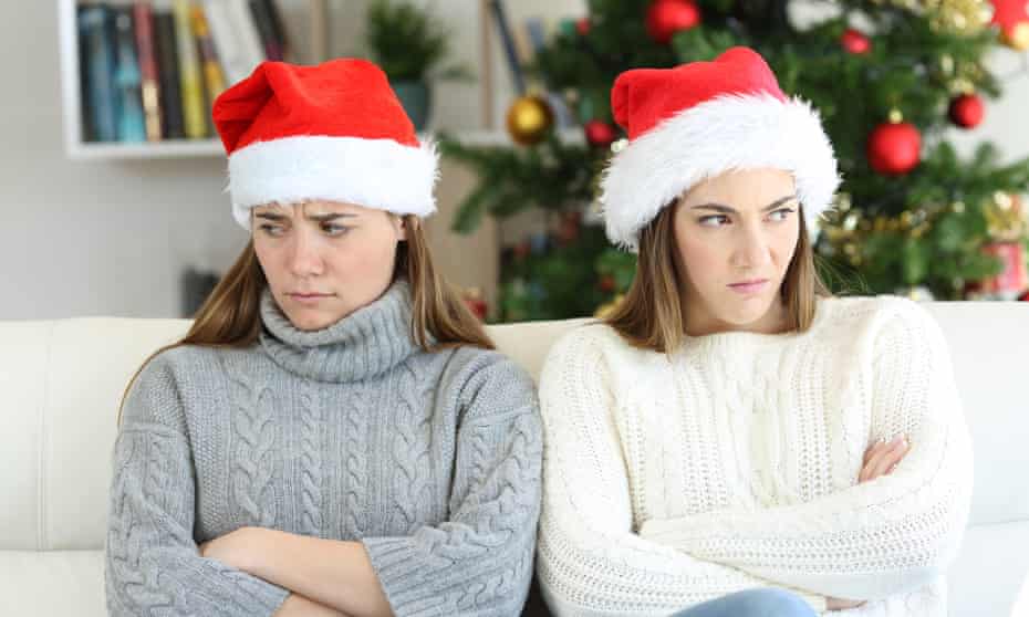 Two women in Santa hats looking glum on a sofa