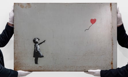 Auctioneers in white gloves hold up Banksy’s Girl with Balloon
