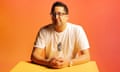 Posed portrait of Sumit Paul-Choudhury sitting at a table, in front of a bright orange background
