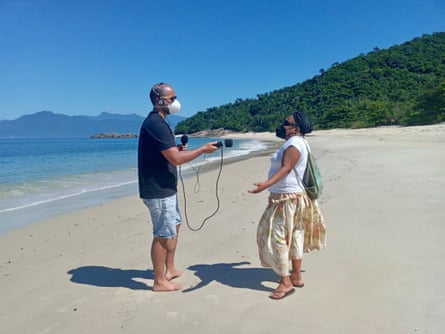 A tall man holds a microphone towards a woman on a sandy beach