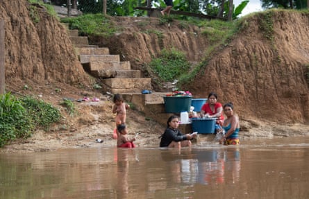 A group of women and children bathes and washes utensils and clothes in a brown river