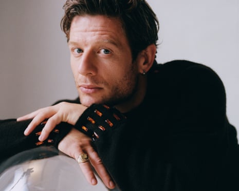 Head shot of actor James Norton, leaning on a big clear ball