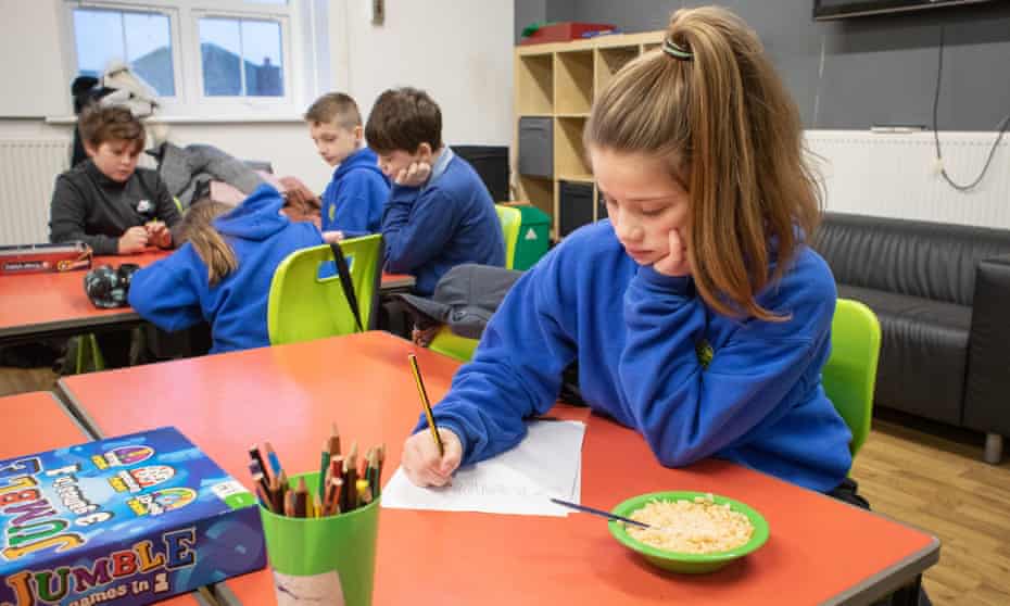 Pupil Hall Storm draws and eats breakfast, while other pupils behind play games and eat breakfast, at Cadoxton Primary School in Barry, South Wales, one of the schools taking part in the trial.
