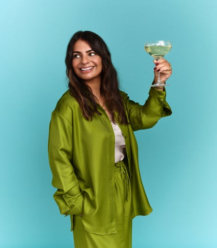 Meera Sodha wing a silky green trouser suit and holding up a champagne saucer