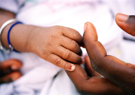Closeup of the hand of an African baby, who is wearing two bracelets, holding an adult’s hand