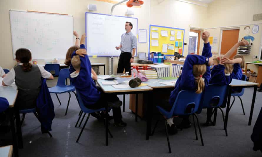 Primary school pupils working in classroom with male teacher.