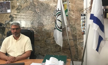 رجل يجلس على مكتب أمام خريطة كبيرة وبجانبه علمان، أحدهما العلم الإسرائيلي 