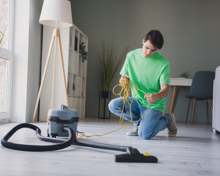 A person is organising the yellow cable of the vacuum cleaner which is on the floor in front of them in a living room.