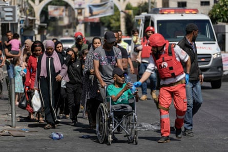 A Red Crescent worker helps residents, including one man in a wheelchair, evacuate the refugee camp in Jenin.