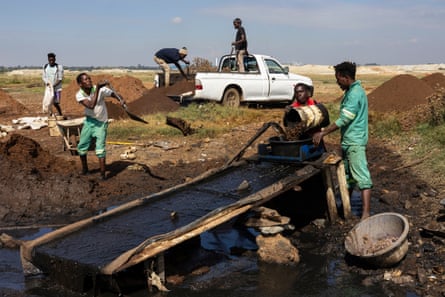 Mineiros despejam terra de baldes em uma bacia no topo de uma rampa onde ela é enxaguada com água de um cano 'Estamos com fome, não há empregos': a desesperada corrida do ouro em um município sul-africano