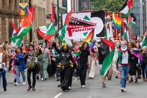 People carrying banners, the rainbow flag and the flag of Palestine walk along a street