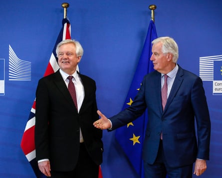 Barnier holds out a hand to Davis, who is looking the other way. They are standing in front of the Union flag and the EU flag