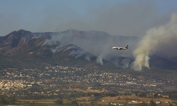 Ryanair plane flying in front of mountains and plumes of smoke rising from them in the distance