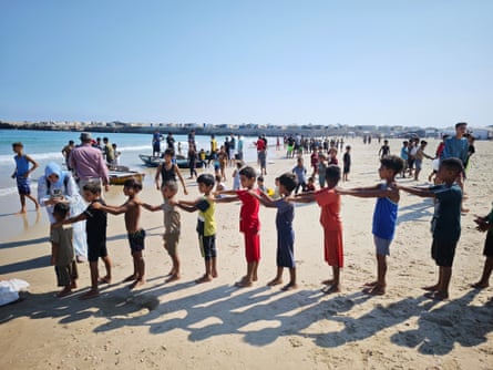 A line of children on a beach with their hands on each other’s shoulders