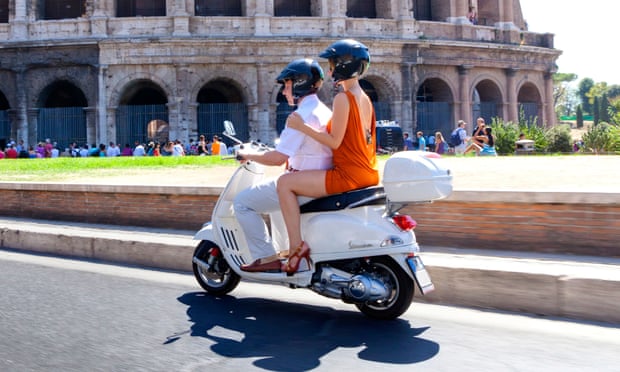 People riding a scooter past the Colosseum in Rome
