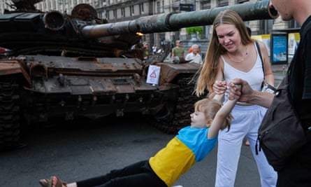 A man and woman hold a child next to destroyed Russian army equipment in the centre of Kyiv