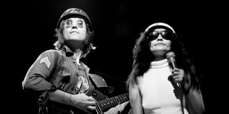 John Lennon, wearing an army hat and jacket, and Yoko Ono, wearing a white dress and hat, on stage